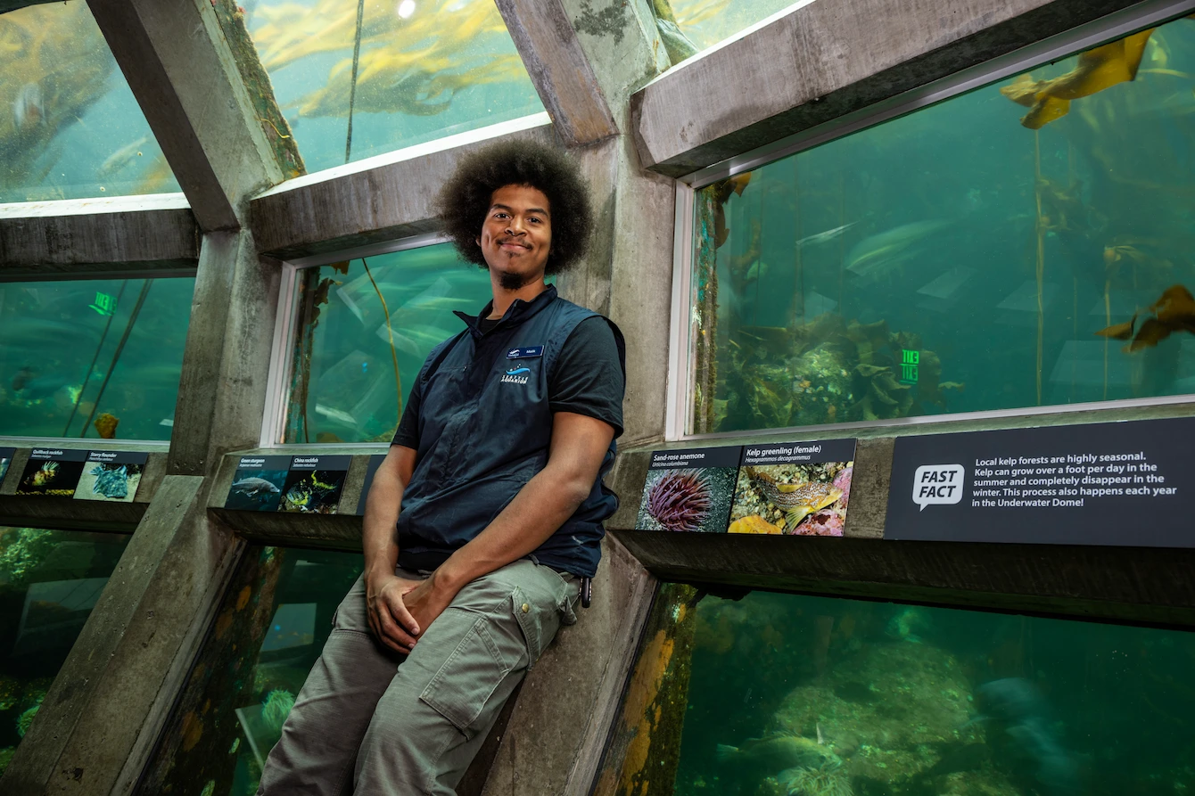 Malik Johnson, a man with dark hair, smiling and leaning against the Underwater Dome habitat.